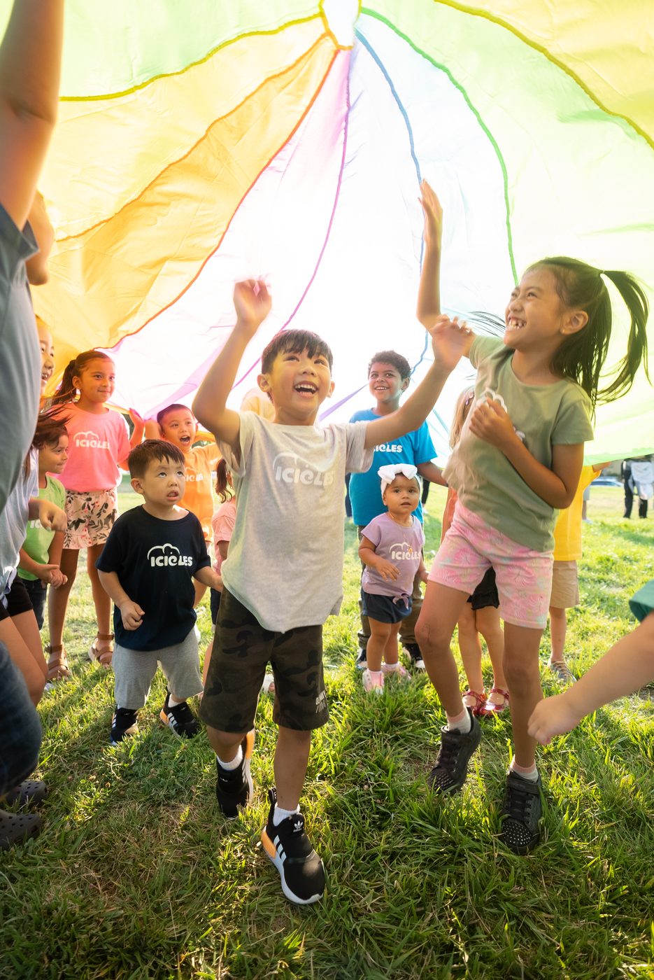 Children playing under a rainbow parachute at an Icicles fundraiser