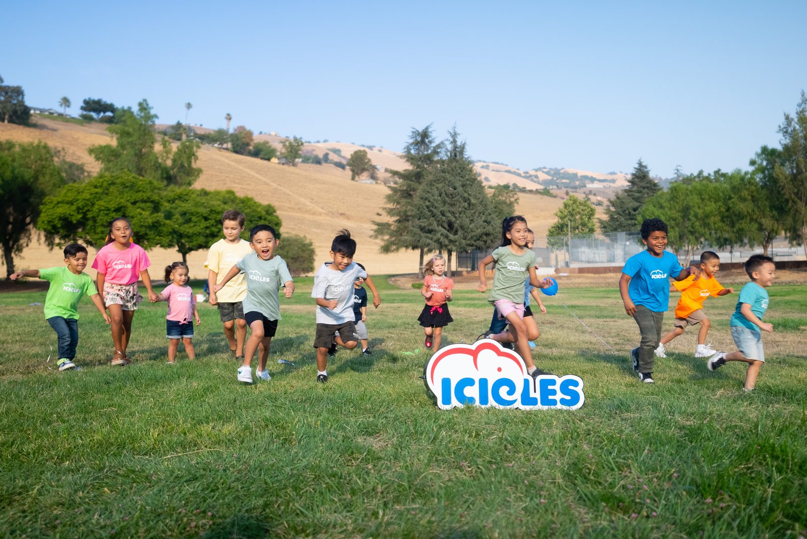 Children in Icicles t-shirts running across a park toward the Icicles logo sign